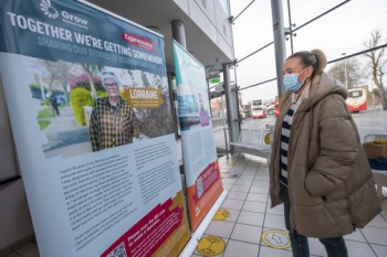 Image shows a Bus Éireann female customer standing in a Bus Station reading information on stands about Grow Mental Health